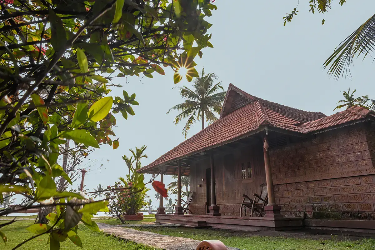 Laterite-walled heritage cottage with a sloped tiled roof beside the backwater